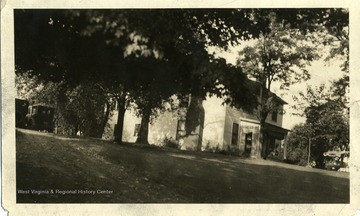An unidentified two-story house is surrounded by trees in Huntington, West Virginia. An automobile is parked near a structure on a dirt gravel driveway.