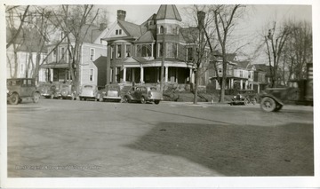 An unidentified house is on a corner of a brick road in Huntington, West Virginia. Several automobiles are parked alongside the road near the front of this house.