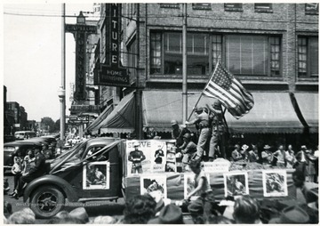 Men in uniform hold up an American Flag on the bed of a truck.