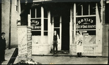 A man holding a baby and two other men stand in front of 'Huntington's premier eating place 'away back when.''