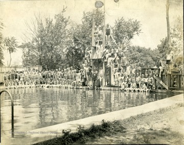 Many children line the pool and the diving boards.