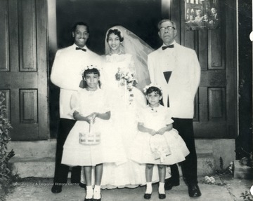 African-American wedding party, two girls, husband and wife, and an elderly gentleman pose for a photograph.