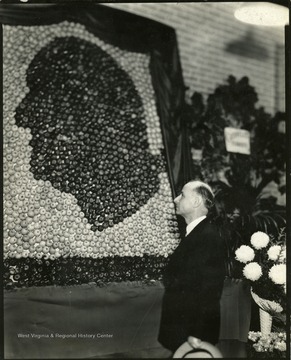 A man stands in profile looking at the apple display shaped like a face.