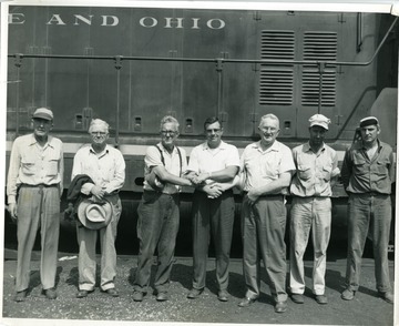 Seven Baltimore and Ohio Train Workers stand in front of a railroad car.