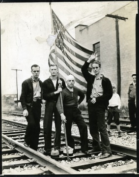 Four men are standing on railroad tracks holding an American flag.