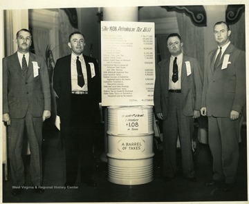 Four men wearing suits standing beside a barrel with the 1938 Petroleum Tax Bill on top of it.  Martinsburg, W. Va.