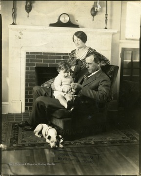 Couple sitting in a chair with a child in the man's lap.  A dog is sitting at the foot of the chair, Martinsburg, W. Va.