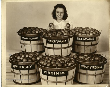 Yvonne Gerbrick, Apple Blossom Queen, standing behind barrels of apples from Maryland, Pennsylvania, Delaware, New Jersey, Virginia, and West Virginia.