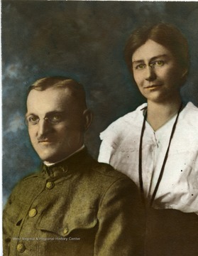 Man is wearing a green uniform, with a lady in a white shirt behind him.