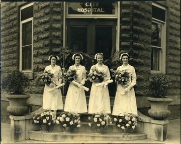 Four nurses in front of the city hospital with bouquets in their hands and baskets of flowers in front of them, Martinsburg, W. Va.