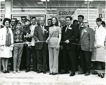 Group of people gathered as a woman wearing a crown prepares to cut a ribbon.