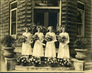 Four nurses in uniform stand with flowers and diplomas.