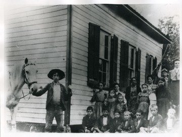 School children and their teacher pose for a group portrait outside school buildin.  'First School in Nitro, Built 1868, Located at the head of Blakes Creek.' 