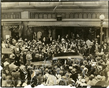 Large crowd of people surrounding a car driving through the town, Martinsburg, W. Va.