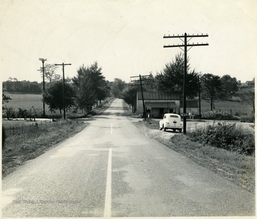 Paved road running through the country side of Martinsburg, W. Va.  Apples advertised for sale at wooden building at intersection.  Also a beer sign on a telephone pole.