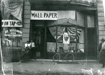 Two men are standing outside the Parkersburg Paint Store which also sells wallpaper. The store is located next to Joe Reitzenberg's Family Liquors Store.