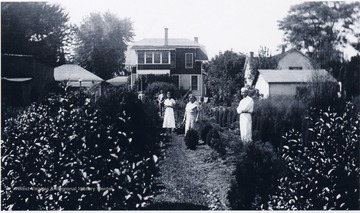 'Charles Thomas Gorby (on right) in his nursery.  663 Maple Avenue New Martinsville, W. Va. Others unknown.  Note the second floor 'sleeping porch' which had six windows, and the chicken coop behind the bird house on tall post at left center.  House in the upper right is the McEldowney home, a pioneer homestead for this area.'