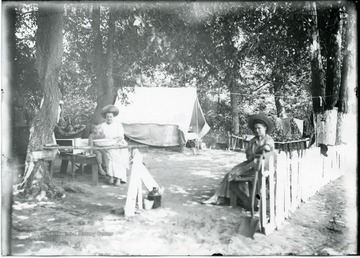 Two women and two boys sit next to a tent at a campsite.