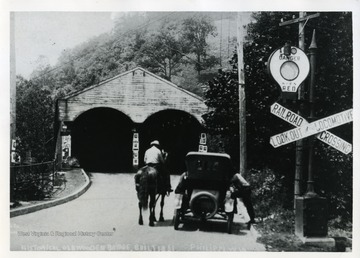 A man on a horse is talking to men in an automobile in front of the Old Wooden Covered Bridge in Philippi. West Virginia.