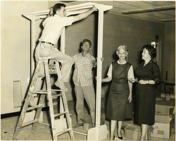 Librarians look on as two men construct shelving unit.