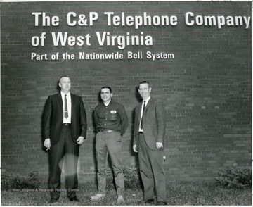 From left to right: Stan Stancowicz, John Morgan, and Howard Husk standing under  sign that reads: The C and P Telephone Company of West Virginia, Part of the Nationwide Bell System.  Morgantown, W. Va.