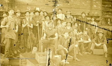 Anton Romisch, second from left standing. Workers pose for photograph. Many of the workers holding tools. 