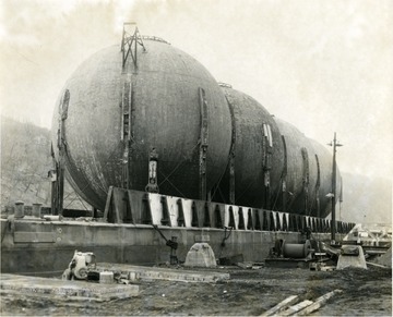 Storage tanks from Morgantown Ordnance Works seen close up. Two men standing on on ladder near the first tank. 