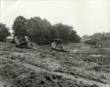 Construction of shopping center on the corner of University Avenue and Patteson Drive located in Morgantown, W. Va. Bulldozers working on ground of construction site. 