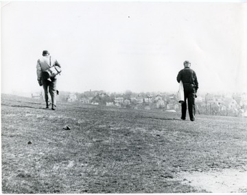Two men carry their golf bags across the green.