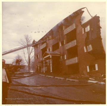 'This picture shows an East Everly Street apartment building which was destroyed by fire on March 20th, 1972. (East Everly Street runs parallel to University Avenue in the vicinity of Pierpont House and the Twin Tower Dorms)  The building was owned by James M. Prete, Morgantown Contractor.  The building contained 15 apartments which housed university students and faculty members.  The fire started at about 12:30 in the afternoon on March 20.  These pictures were shot at about 6:00 in the evening just before the fire was brought under control.  The fire was apparently caused by a spark from the torch of a welder who was working in the attic of the building.  The insulation was ignited and the fire spread down through the walls and across the roof.  The fire provoked a controversy in city council concerning the adequacy of Morgantown's fire fighting equipment.  Mr Prete was also accused of using cheap and unsafe methods in the construction of the building.  These pictures were shot by Miss Carol Wrobleski who lived on Harding Avenue near the site of the fire.'