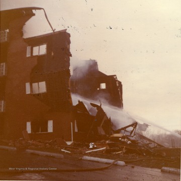 'This picture shows an East Everly Street apartment building which was destroyed by fire on March 20th, 1972. (East Everly Street runs parallel to University Avenue in the vicinity of Pierpont House and the Twin Tower Dorms) The building was owned by James M. Prete, Morgantown Contractor. The building contained 15 apartments which housed University students and faculty members. The fire started at about 12:30 in the afternoon on March 20. These pictures were shot at about 6:00 in the evening just before the fire was brought under control. The fire was apparently caused by a spark from the torch of a welder who was working in the attic of the building. The insulation was ignited and the fire spread down through the walls and across the roof. The fire provoked a controversy in city council concerning the adequacy of Morgantown's fire fighting equpiment. Mr. Prete was also acused of using cheap and unsafe methods in the construction of the building. These pictures were shot by Miss Carol Wrobleski who lived on Harding Avenue near the site of the fire.'