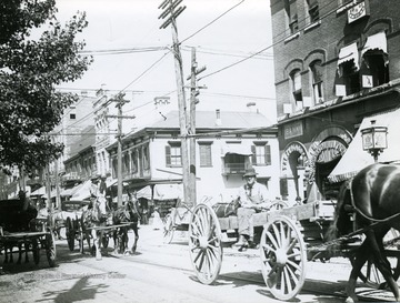 'High Street scene, many years ago'. People seen riding in horse-drawn wagons. Near the Bank on High Street in Morgantown, W. Va. 