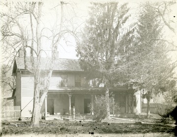 The Loughead House located in Morgantown, W. Va. seen here. In front of the house stands a few trees. Also, in front of the house a water pump can be seen. 