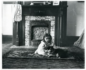 A girl is sitting with a black and white cat in front of a fireplace in a house in Morgantown, West Virginia.