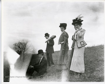 Three women, two men standing on a hillside.  One woman is holding a camera. 