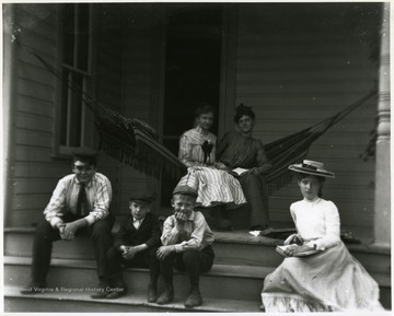 Two girls seated in a hammock, while three boys and a young girl sit on the steps.