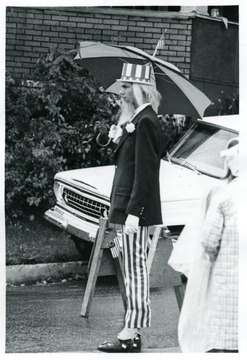Man dressed as Uncle Sam holds an umbrella and watches the parade.