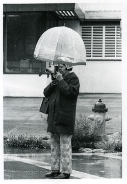 Woman with an camera takes a picture from under her umbrella.