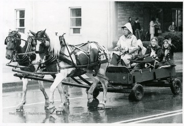 Horses pull a man and three girls in a small wagon.