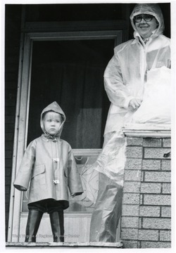 A woman and a small girl watch the parade in their raincoats.