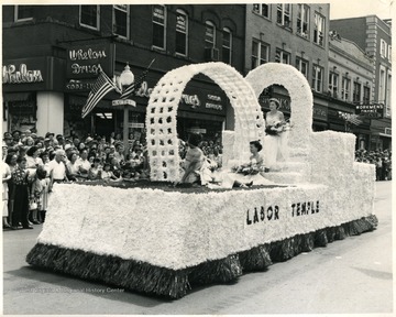 Three ladies in dresses sit on the Labor Temple float.