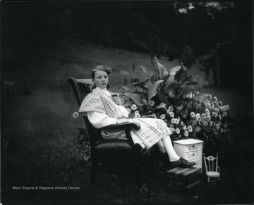 A girl is sitting in a chair outdoors near a large flower bed in Morgantown, West Virginia.