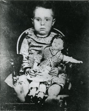 An unidentified child seated in a chair holdind a doll. 