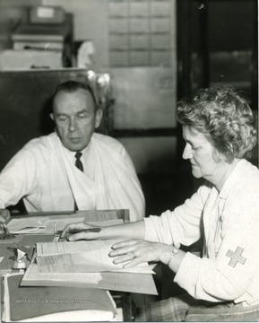 Man with a sling on his arm seated at a table with a health care worker.
