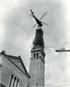 'The 600-pound bronze angel statue is slowly lowered onto the tower of the 175-foot church at Sacile, near Udine by a SETAF H-34 Helicopter of the 202nd Army Aviation Company. The helicopter is piloted by Captain William M. Strawn, Jr, and 1st Lieutenant Ramon F. Warner, while SP2 Richard L. Boyd, inside the craft directed the Army crew and Italian workmen in the delicate task. The 16th Century tower originally bore a wooden angel which was destroyed by earthquake and bombardment. 16 August 1957.' 'Please Credit U.S. Army Photograph.' 