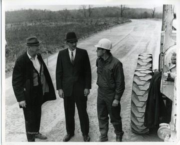 John C. Solomon (second from left) and other road crew members stand in front of a tractor while talking.