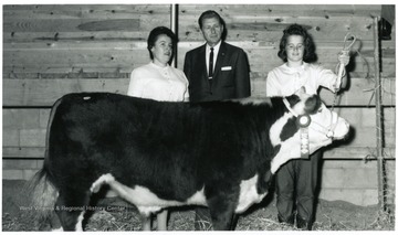 Clem Peets stands next to his daughter who is holding the reigns of the cow.