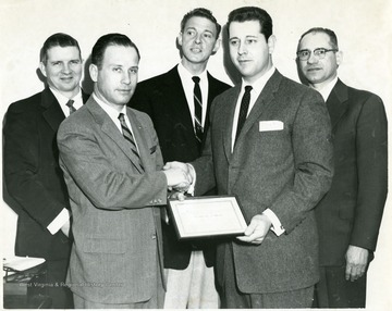 Two men shake hands as one is presented with a certificate of merit.