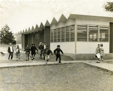 View of the addition to Suncrest Grade School 'done in green and yellow' with children running along side.  Girl in dark coat, fourth from left is Nancy Claire Eddy.