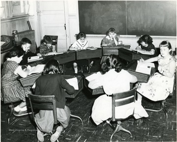 View of fourth and fifth grade children sitting a circle in a classroom.  Far left is Ruth Bard, left with back to camera is Suzy Pauley, right front with back to camera is Jennifer Jacobs, far right is Susan Brown, then right to left are Becky Singleton, Roberta Malott, Marta Eicker, Danny Brennan, and Lynn Spangler. 
